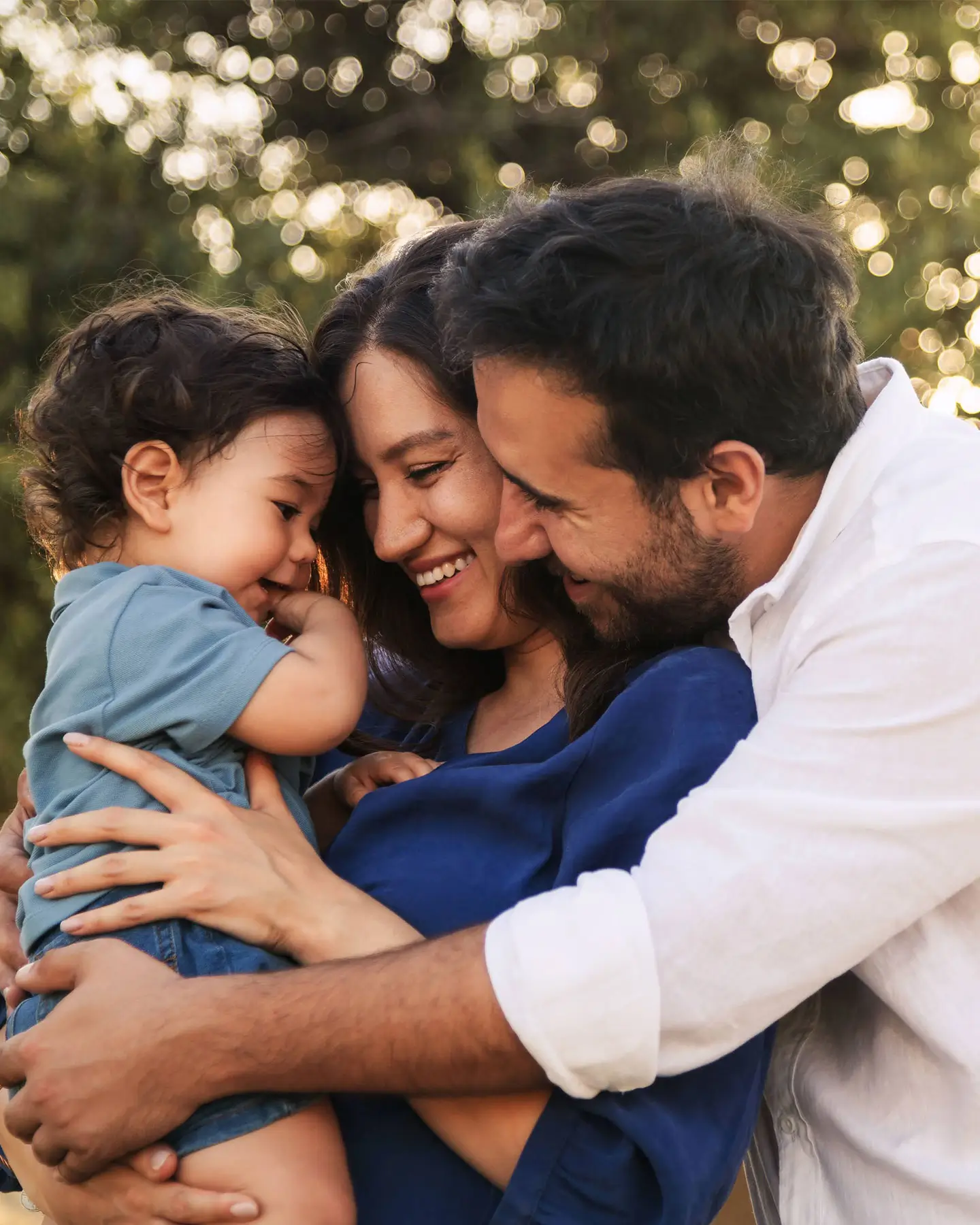 a mother holding her child face to face with the dad behind her giving them both a hug